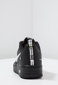 Černé tenisky Nike s texturovaným svrškem, bílými akcenty a ikonickým logem na patní části. Texturovaná podrážka s nápisem "AIR".