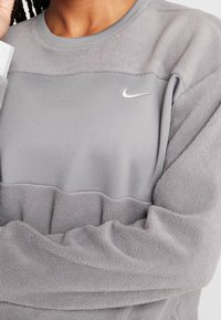 Grå fleece sweatshirt med en glat, lysegrå overdel og en tekstureret underdel. Har et lille hvidt Nike-logo på brystet.