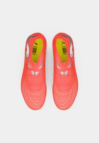 Botas de fútbol de coral brillante con superficie texturizada, detalles en gris y un interior amarillo neón. Cuentan con un diseño aerodinámico y cierre con cordones.
