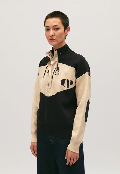 Pull en tricot beige et marine avec un col haut, patte de boutonnage mi-longue et motifs noirs contrastants. Texture douce et coupe décontractée.