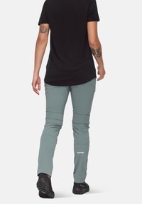 Pantalons de randonnée légers et gris avec des poches zippées et un tissu texturé. Associés à une chemise noire à manches courtes et des chaussures noires.