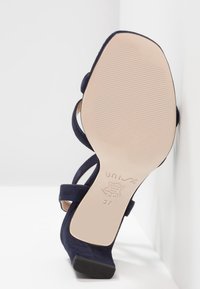 Sandale à talons hauts en suède bleu marine avec une arrière ouvert, des brides de cheville et une semelle en caoutchouc. Présente un logo de marque en relief sur la semelle intérieure. Taille 37.
