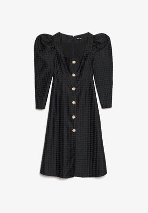 Must kleit puffvarrukatega, tekstureeritud kangast ja põlveni ulatuva lõikega. Esiküljel on kuus kuldse tooniga nuppu.