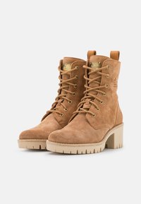 Bottines en suède beige avec un talon haut, un devant à lacets, des œillets en métal et une languette à l'arrière. Semelle en caoutchouc surélevée avec adhérence.