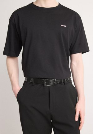 Black short-sleeve t-shirt made of cotton, featuring a round neckline and small pink "BOSS" logo on the left chest. Worn with black pants and belt.
