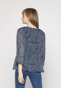 Blusa azul-escura com um padrão ondulado, tecido leve, bainha peplum e mangas três quartos. A parte de trás apresenta um pequeno fecho de botão.