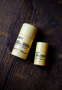 Dwa naturalne dezodoranty w cylindrycznych opakowaniach, jedno duże i jedno małe, oba żółte z minimalistycznym tekstem w kontrastowych kolorach.