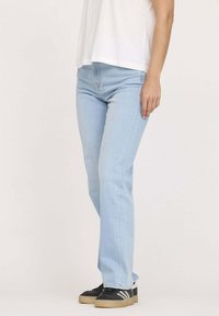 Jeans en denim bleu clair avec une coupe droite, présentant un design classique à cinq poches et des détails de couture subtils, associés à des baskets noires.