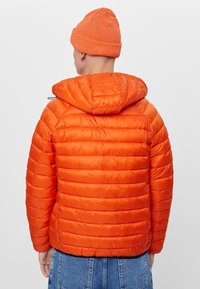 Oranžová bunda s péřovou podšívkou, horizontální prošívání, připevněná kapuce a hladký povrch. Nosit s odpovídající pletenou čepicí.
