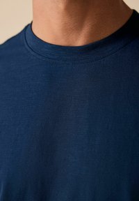 Camiseta azul marino con cuello redondo, fabricada en un tejido suave y ligeramente texturizado. Se ven pocas costuras cerca del cuello.