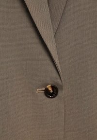 Rjav karo blazer tkanine z teksturiranim koncem, ki se ponaša z izrazitim temnim gumbom in dizajnom z vidno klapno.