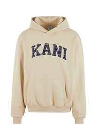 Beige hoodie gjord av mjukt material med en känguruficka, med en stor, marinblå "KANI" grafik över bröstet.