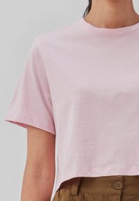 Lyserød cropped t-shirt lavet af bomuld. Korte ærmer, rund hals og glat struktur. Nederste kant falder over taljen, parret med khaki bukser.