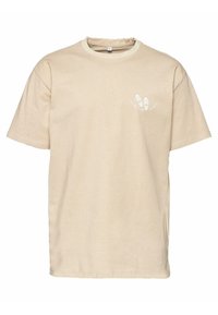 Beige pamut póló kerek nyakkal, rövid ujjakkal, és egy nyomott mintával, amely lábnyomokat és szöveget tartalmaz a bal mellrészen.
