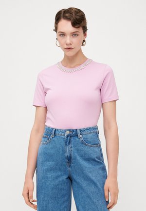 Rosa t-skjorte med korte ermer som har en dekorativ halslinje med perle-accenter, kombinert med høyt midje blå denimbukser.