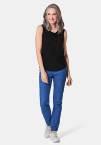 Top nero senza maniche, jeans blu aderenti e sneakers chiare. Il top ha un collo morbido e drappeggiato; i pantaloni sono in denim con dettagli minimi.