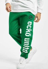 Grønne sweatpants med hvid "eckō united" tekst og logo, med en afslappet pasform og blødt stof. Bæres med hvide sneakers.