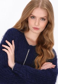 Sötétkék, bolyhos pulóver, kerek nyakkal, texturált mintázattal és világosszürke díszítéssel a nyakrészen és az ujjakon.