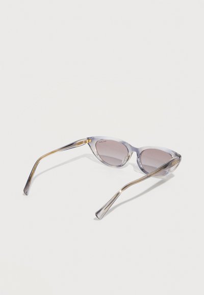 Διαφανή γκρι γυαλιά ηλίου σε σχήμα ματιού γάτας με φακούς διαβάθμισης, εμφανιζόμενα από πίσω σε λευκό φόντο.