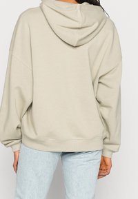Hoodie beige surdimensionné avec capuche à cordon de serrage, poignets et ourlet côtelés. Texture douce, coupe décontractée et détails de couture minimalistes.