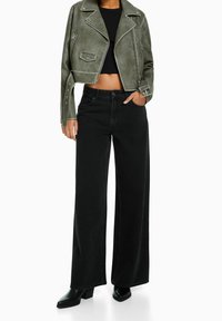 Oříznutá olivově zelená kožená bunda se stříbrnými detaily, v kombinaci s vysokými černými širokými džíny a černými kotníkovými botami na blokovém podpatku.