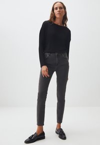 Haut à manches longues noir associé à un jean gris slim fit et des mocassins noirs. Les caractéristiques incluent un col rond et des détails de couture subtils.