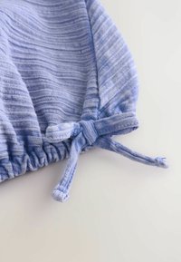 Tissu bleu clair avec un subtil motif rayé, présentant une bande élastiquée et un détail de cordon à nouer pour un ajustement réglable.