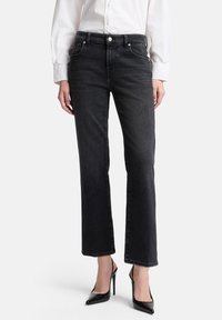 Czarne jeansy o prostych nogawkach z klasycznym designem pięciu kieszeni, srebrnymi okuciami i subtelnym przetarciem, zestawione z eleganckimi czarnymi szpilkami i białą koszulą.