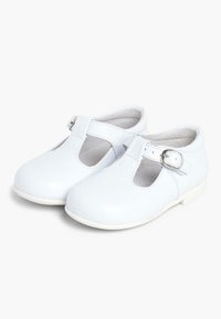 Witte leren T-bar schoenen met een band en gesp, ronde neuzen en geperforeerde details aan de zijkanten, rustend op een witte zool.