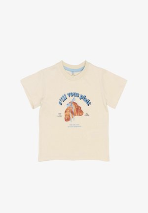 Cremfarbener Baumwoll-T-Shirt mit einem Croissant-Graphic, einem blauen Band, blauer Schrift und einem runden Ausschnitt mit kurzen Ärmeln.