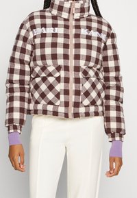 Brązowa i kremowa puchowa kurtka w kratę z wysokim kołnierzem, zamkiem błyskawicznym z przodu, dwiema naszytymi kieszeniami i fioletowymi ściągaczami.