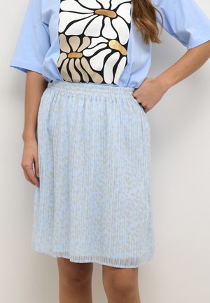 Lichtblauwe geplooide rok met subtiele beige vlekjes, gecombineerd met een lichtblauw T-shirt met grote gestileerde witte en beige bloemmotieven.