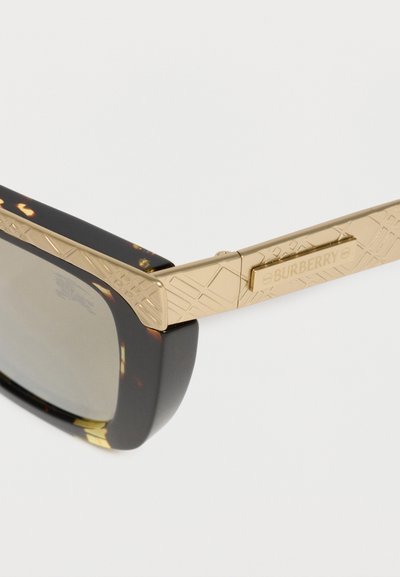 Γυαλιά ηλίου με σκούρα φιλικά πλαίσια και χρυσούς υφασμένους βραχίονες με το λογότυπο Burberry στο πλάι.