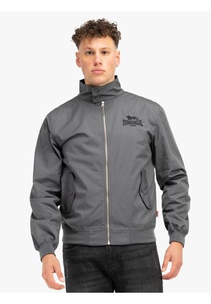 Chaqueta bomber gris con cierre de cremallera, cuello alzado, dos bolsillos laterales y detalle del logo en el pecho. Fabricada con un material liso y resistente.