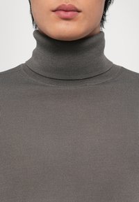 Pulover gri cu guler înalt din material ribbed, caracterizat printr-o croială strânsă, cu o textură fină și fără modele vizibile.