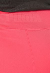 Różowe legginsy sportowe z prążkowanym paskiem w talii. Materiał wydaje się gładki i elastyczny, z płaskimi szwami dla wygody i trwałości.