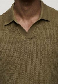 Oliwkowy sweter z dzianiny o prążkowanej fakturze, krótki kołnierz i dekolt w kształcie litery V. Brak widocznych wzorów lub ozdób.