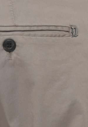 Primo piano di tessuto beige con un bottone nero a quattro fori e un piccolo cursore in metallo con la lettera "D".