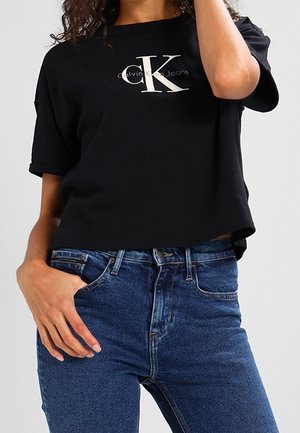 Czarny T-shirt z krótkim rękawem z białym logo "CK" oraz napisem "Calvin Klein Jeans". Połączony z niebieskimi jeansami z wysokim stanem.