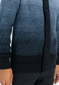 Strickjacke mit einem Farbverlaufsmuster in Blautönen, mit einer dunklen Knopfleiste, gerippten Bündchen und seitlichen Taschen mit schwarzen Knöpfen.