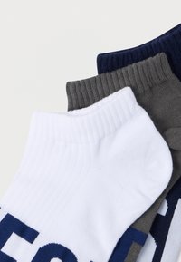 Trys kojinių poros: baltos, pilkos ir tamsiai mėlynos. Kiekvienos viršuje yra ribuotas manžetas, o šonuose – ryškus užrašas. Minkšta medžiaga be siūlių ant kojų pirštų.