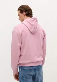 Hoodie in lichtroze, gemaakt van zachte stof. Voorzien van een kangoeroezak en geribbelde manchetten. Gestyled met vervaagde blauwe jeans.