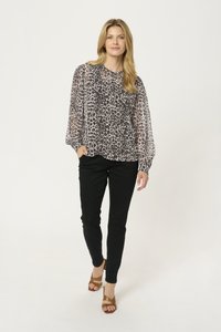 Blouse à imprimé animal avec de longues manches ballons, associée à un pantalon noir slim et des talons bruns à lanières, sur un fond clair.