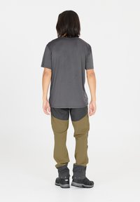 Chemise grise à manches courtes, associée à un pantalon olive et noir avec des accents au niveau des genoux, complétée par des bottes noires. Texture lisse dans l'ensemble.