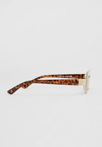 Lunettes de soleil rondes avec une monture en métal doré et des branches en plastique à motif écaille. Elles présentent des extrémités courbées et un logo discret à l'intérieur.
