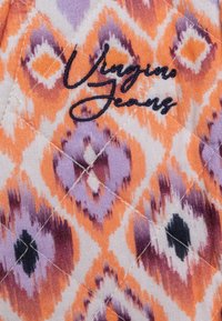 Bavlněná látka s barevným vzorem ikat v oranžové, fialové a bílé barvě s černými akcenty. Obsahuje text "Vangino Jeans" v tmavém prošívání.