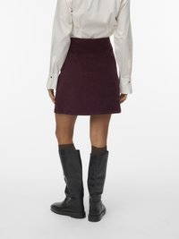 Saia mini de veludo cotelê bordô com cintura alta, combinada com botas de couro pretas até o joelho e meias castanhas escuras.
