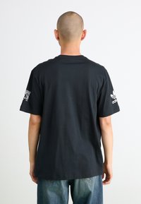 Sort bomuld T-shirt med korte ærmer, rund halsudskæring og hvidt Adidas-logo på venstre ærme. Bagview, stylet med løse denimjeans.