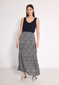 Navy Tanktop kombiniert mit einem langen, fließenden Rock in Schwarz-Weißen Muster. Das Outfit wird mit lässigen weißen Turnschuhen abgerundet.