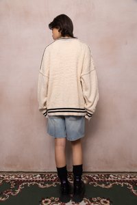 Suéter de gran tamaño en textura cremosa con rayas negras en el dobladillo, combinado con pantalones cortos de mezclilla azul claro y botas de plataforma negras.